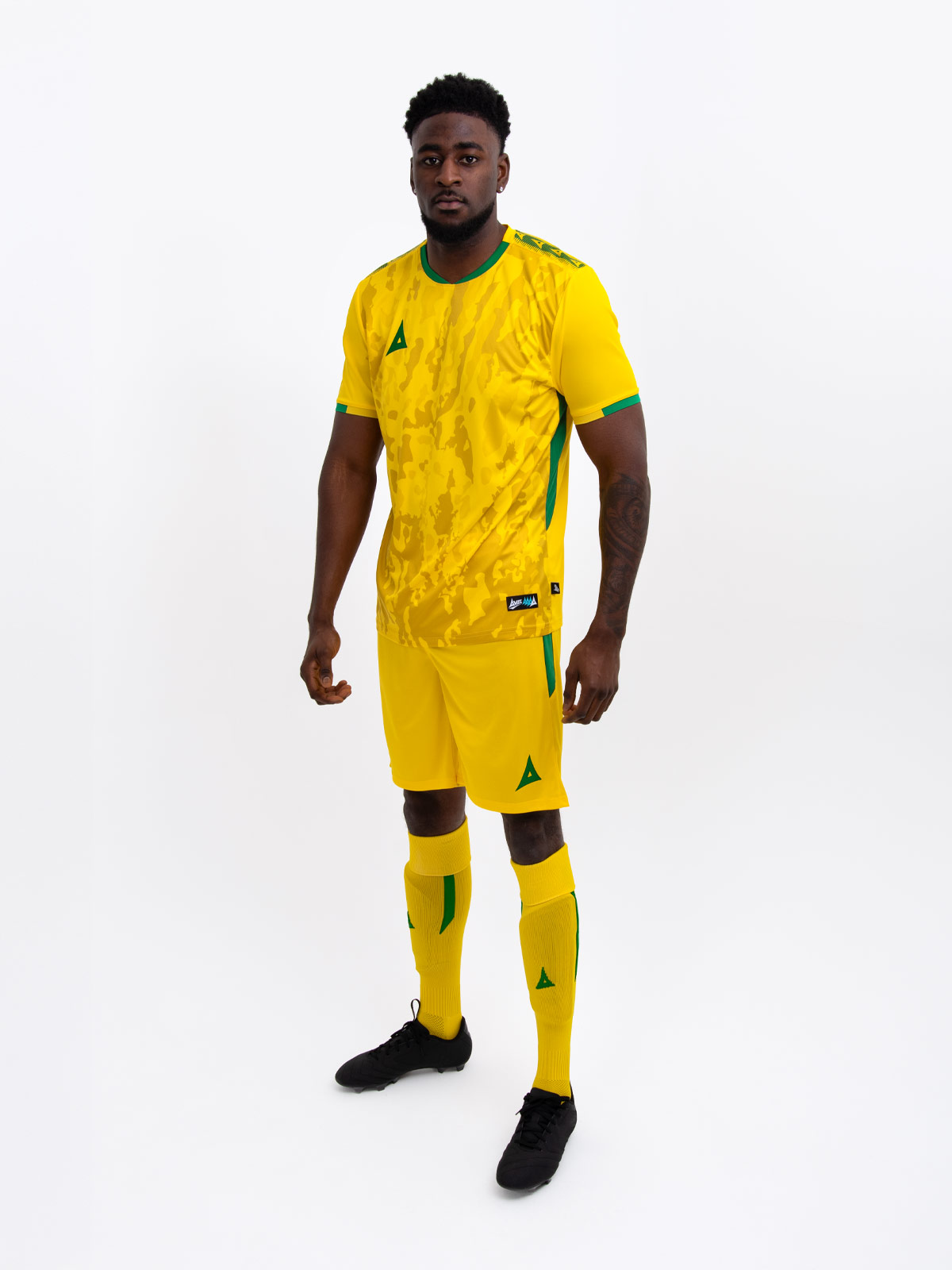a model standing up wearing a yellow football shirt, yellow shorts and yellow football socks with green accent details