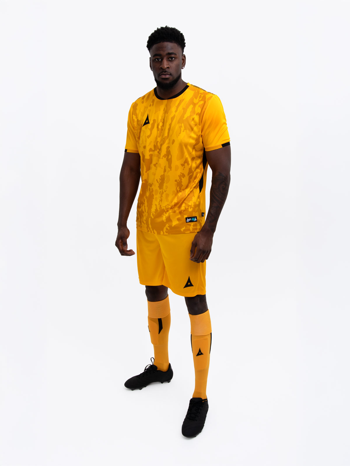 a model standing up wearing an amber and black football shirt, amber shorts and amber football socks.