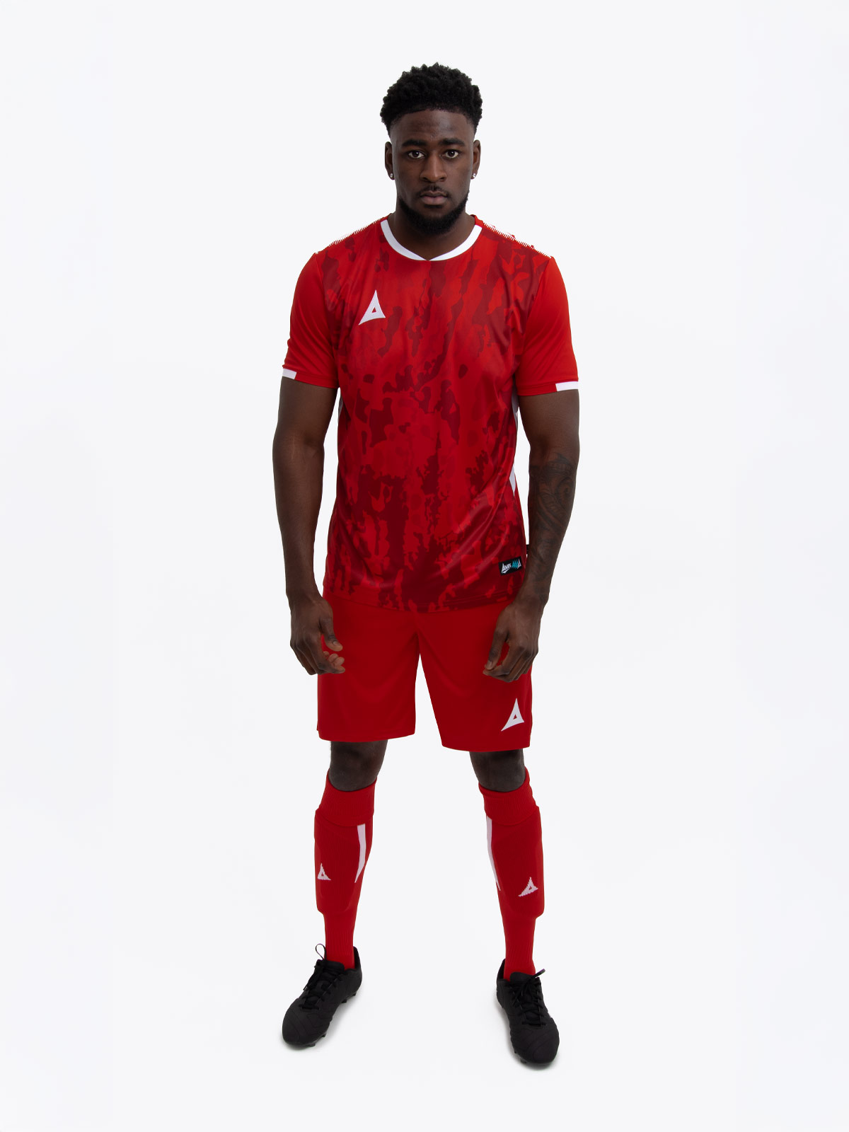 a man standing up wearing a red football shirt, matching red shorts and red football socks.
